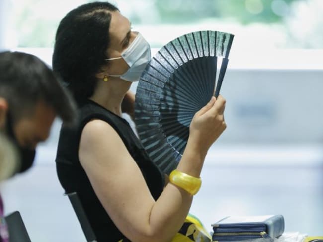 Una mujer con mascarilla se abanica