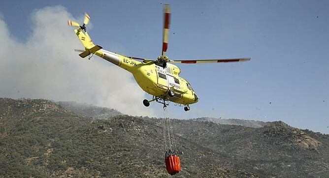 Un helicóptero lleva agua para arrojar sobre el incendio que se inició en la Sierra de Gredos, a la altura del municipio de El Real de San Vicente.