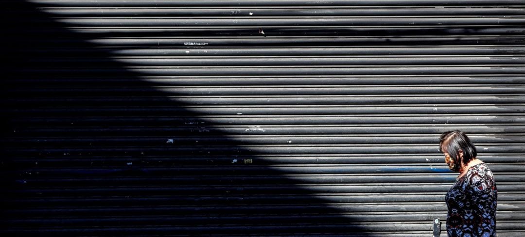  Una mujer con mascarilla camina frente a una tienda cerrada