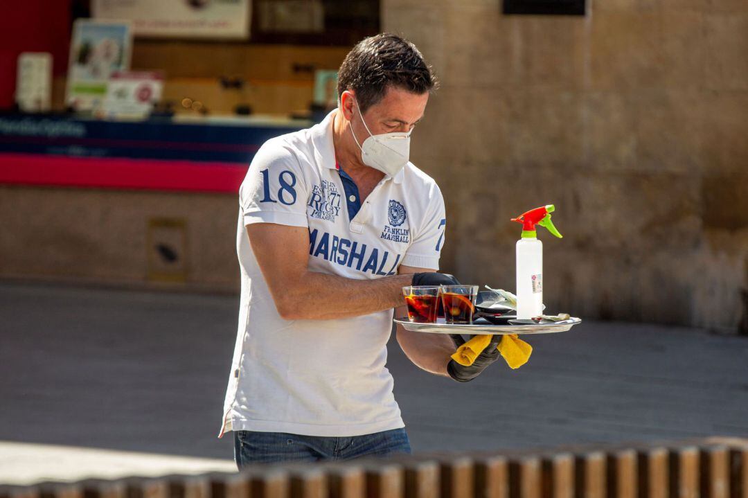 Un camarero atiende una mesa equipado con mascarilla y con un espray desinfectante en el centro de Vitoria