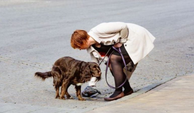 Una señora recogiendo las heces de su perro