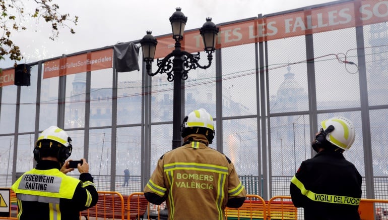 Un bombero alemán (i), uno valenciano y uno italiano (d), contemplan el disparo de la última Máscleta oficial de las Fallas 2018 disparada hoy en la plaza del Ayuntamiento.