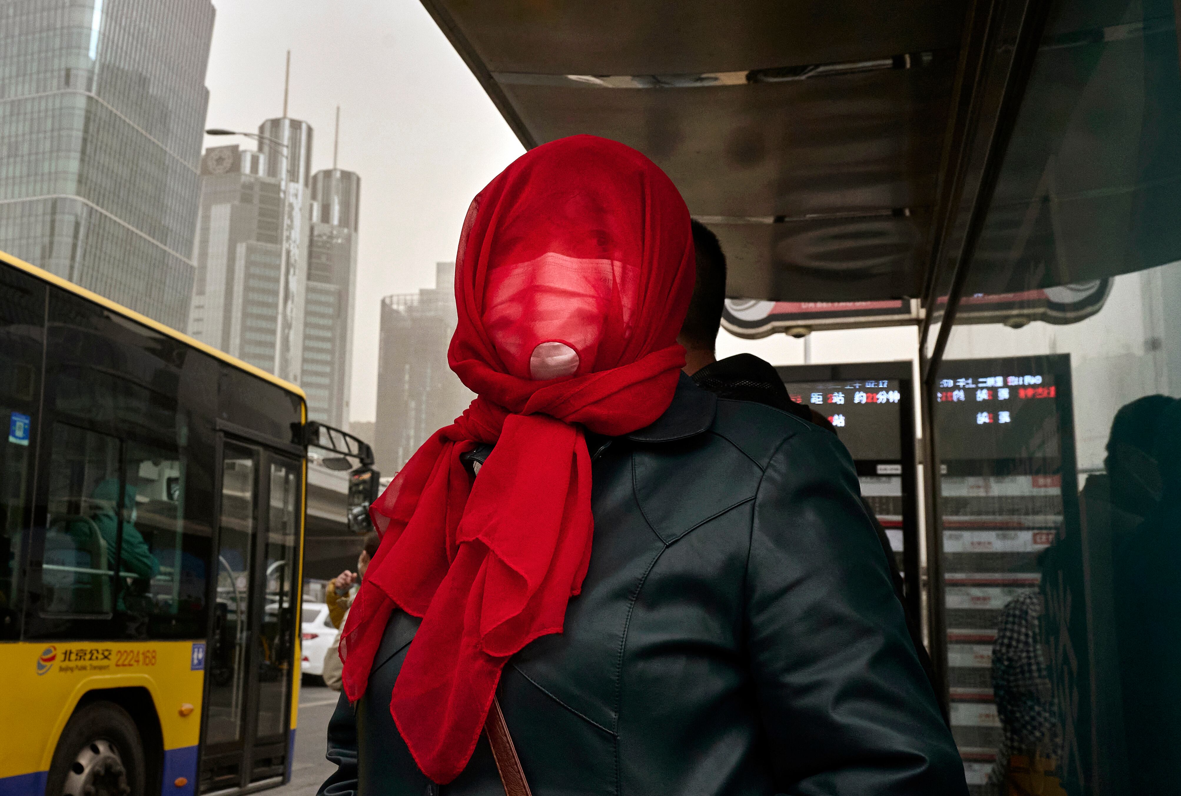 Una mujer se protege mientras espera al bus en Pekín.