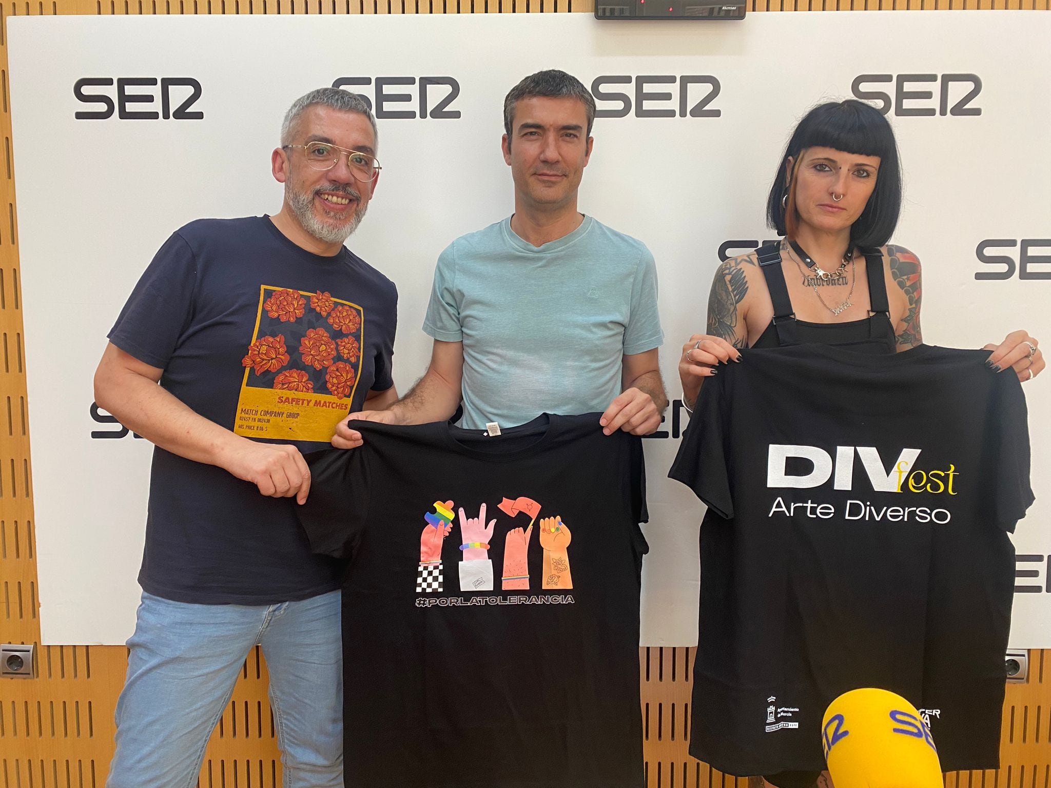 De izquierda a derecha: Paco Sánchez, responsable de Hoy por hoy Murcia, Lorenzo Tomás, presidente de la Junta Municipal de Distrito Centro-Este, y Tanya Vondee, CEO de LaHiperactiva Estudio, con las camisetas preparadas con motivo del Orgullo LGTBI 2023