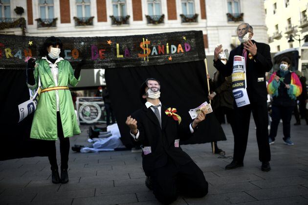 Tres personas, dos de ellas con máscaras del consejero madrileño de Salud, Enrique Ruiz Escudero (d) y del consejero de Hacienda, Javier Fernández-Lasquetty (centro), realizan una &#039;performance&#039; durante una concentración del colectivo ‘Sanitarios Necesarios’ en defensa de la sanidad pública en la Puerta del Sol, en Madrid (España)