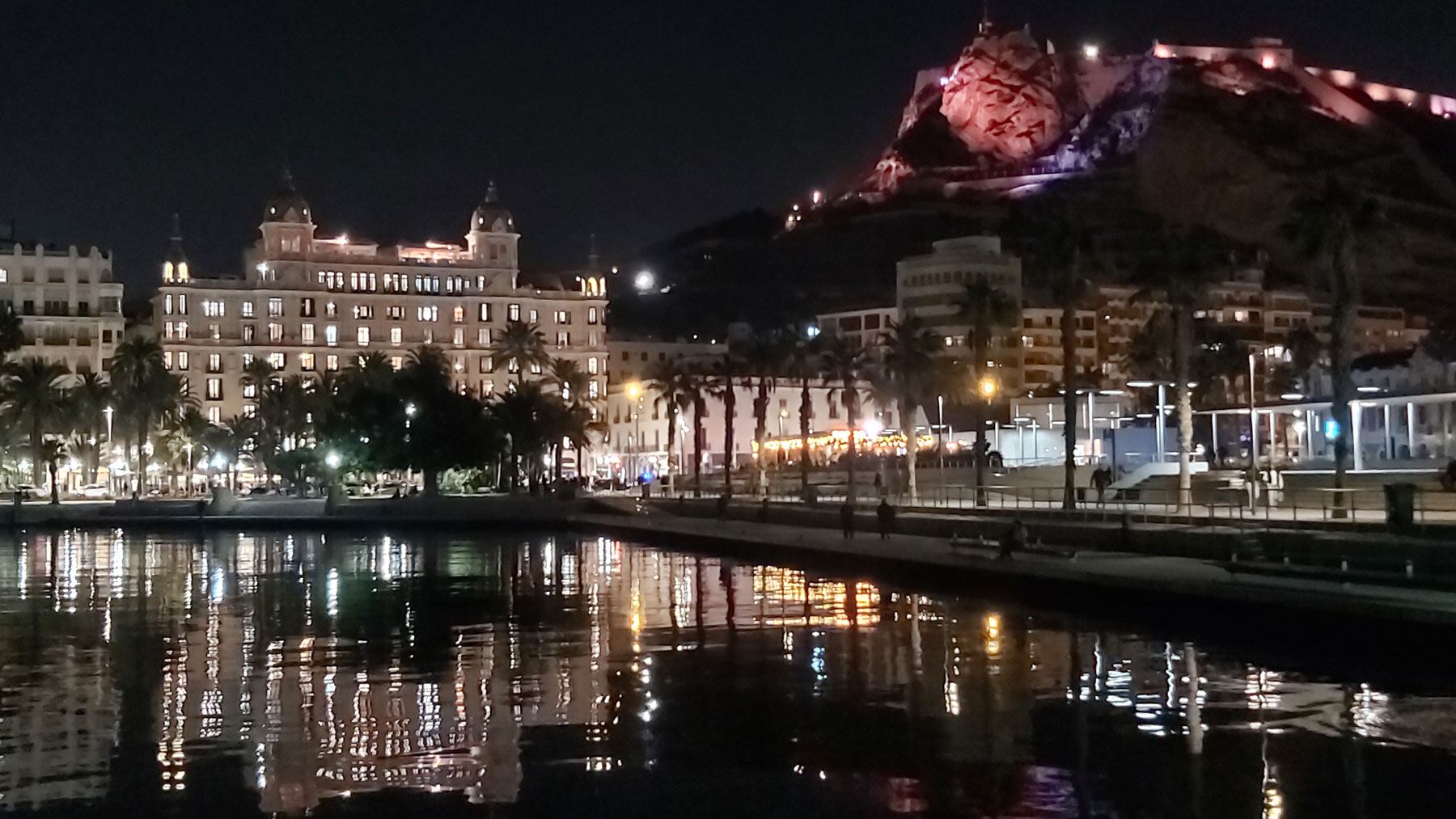 Vista general de la Casa Carbonell iluminada desde el puerto con el castillo de Santa Bárbara al fondo