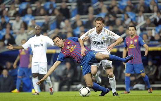 El centrocampista del F. C. Barcelona, Sergio Busquets , cae ante la entrada del jugador del Real Madrid, Xavi Alonso, durante el encuentro correspondiente a la ida de los cuartos de final de la Copa del Rey, que ambos equipos disputan esta noche en el es