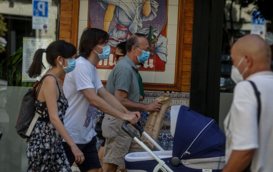 Transeúntes con la mascarilla puesta pasean por la calle.
