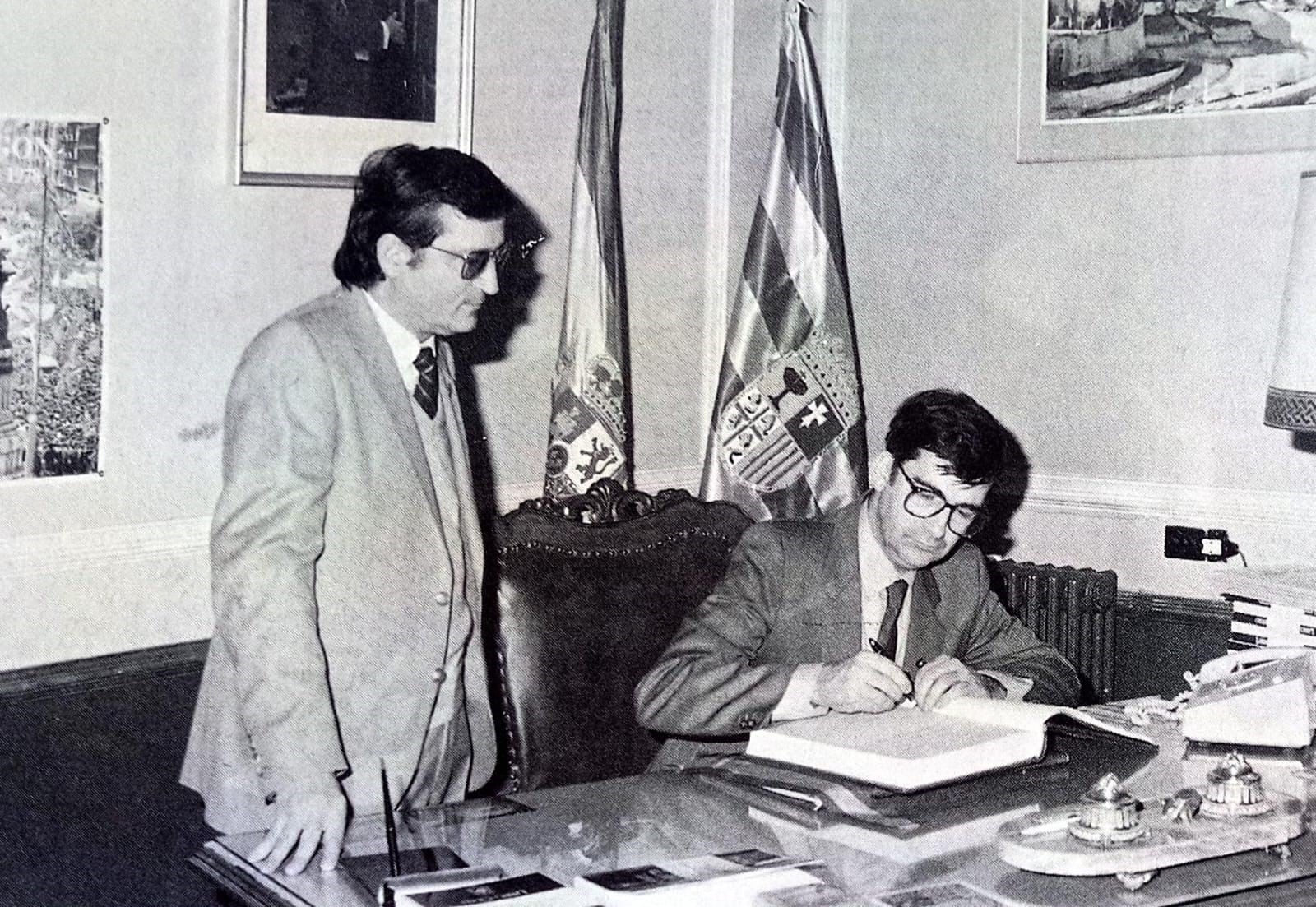 Ernest Lluch firmando en el libro de oro del ayuntamiento con la presencia del alcalde, Francisco Viu.