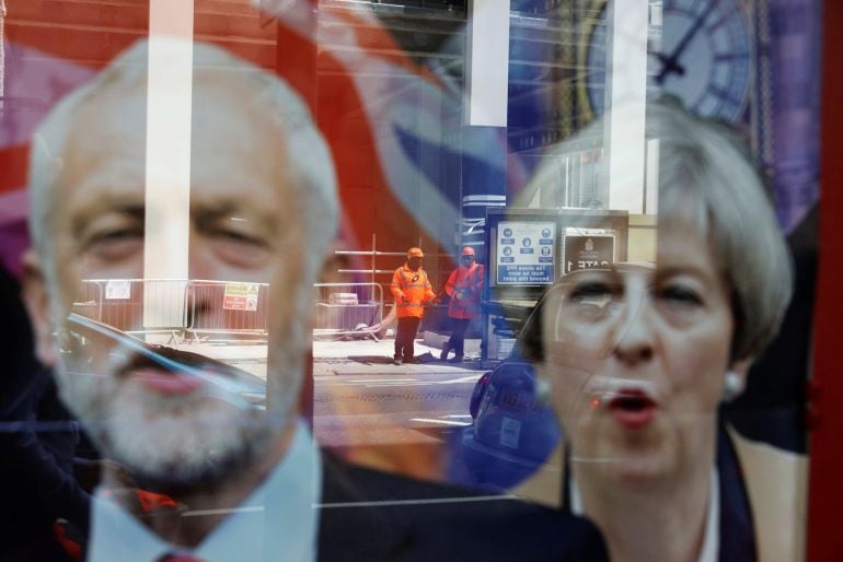 Trabajadores reflejados en una ventana sobre los carteles electorales de Theresa May y Jeremy Corbyn