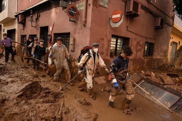 Valencia - Voluntarios caminan por el barro en la calle mientras el área se recupera de las inundaciones generalizadas por la DANA