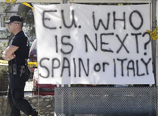 Un policía camina junto a una pancarta en la que se puede leer &#039;Unión Europea, ¿Quién es el siguiente? España o Italia&#039; frente al Parlamento en Nicosia