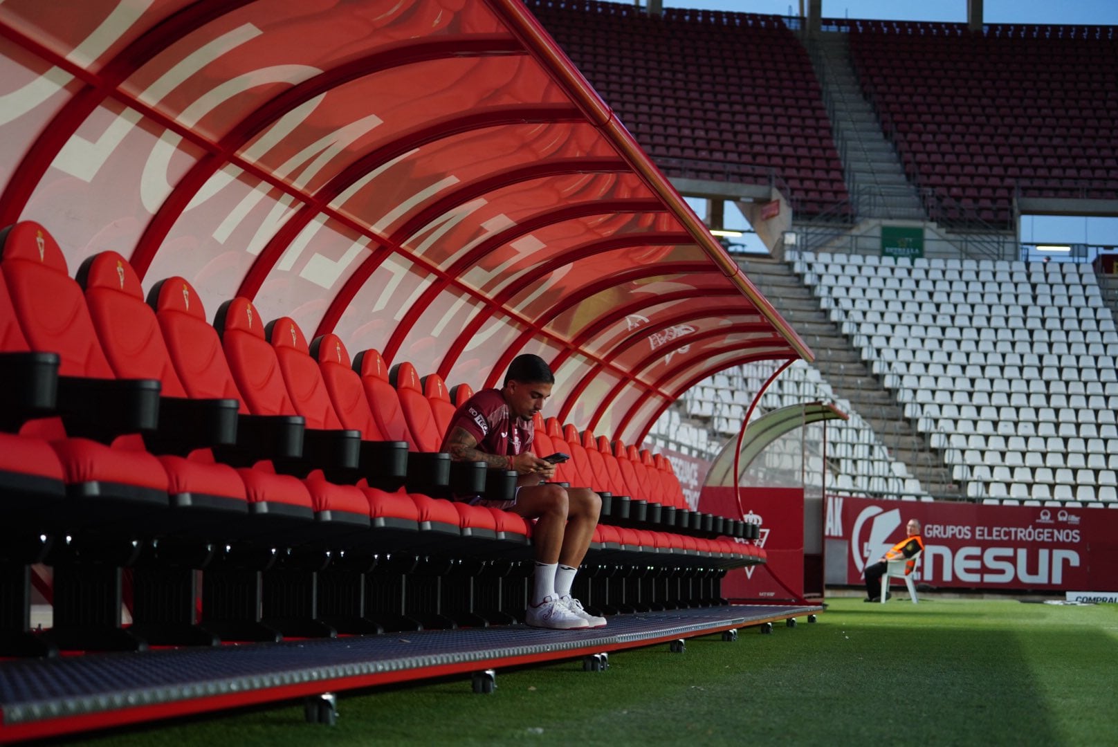 El nuevo banquillo del Real Murcia con Cristo Romero, jugador del primer equipo, concentrado con su teléfono móvil.