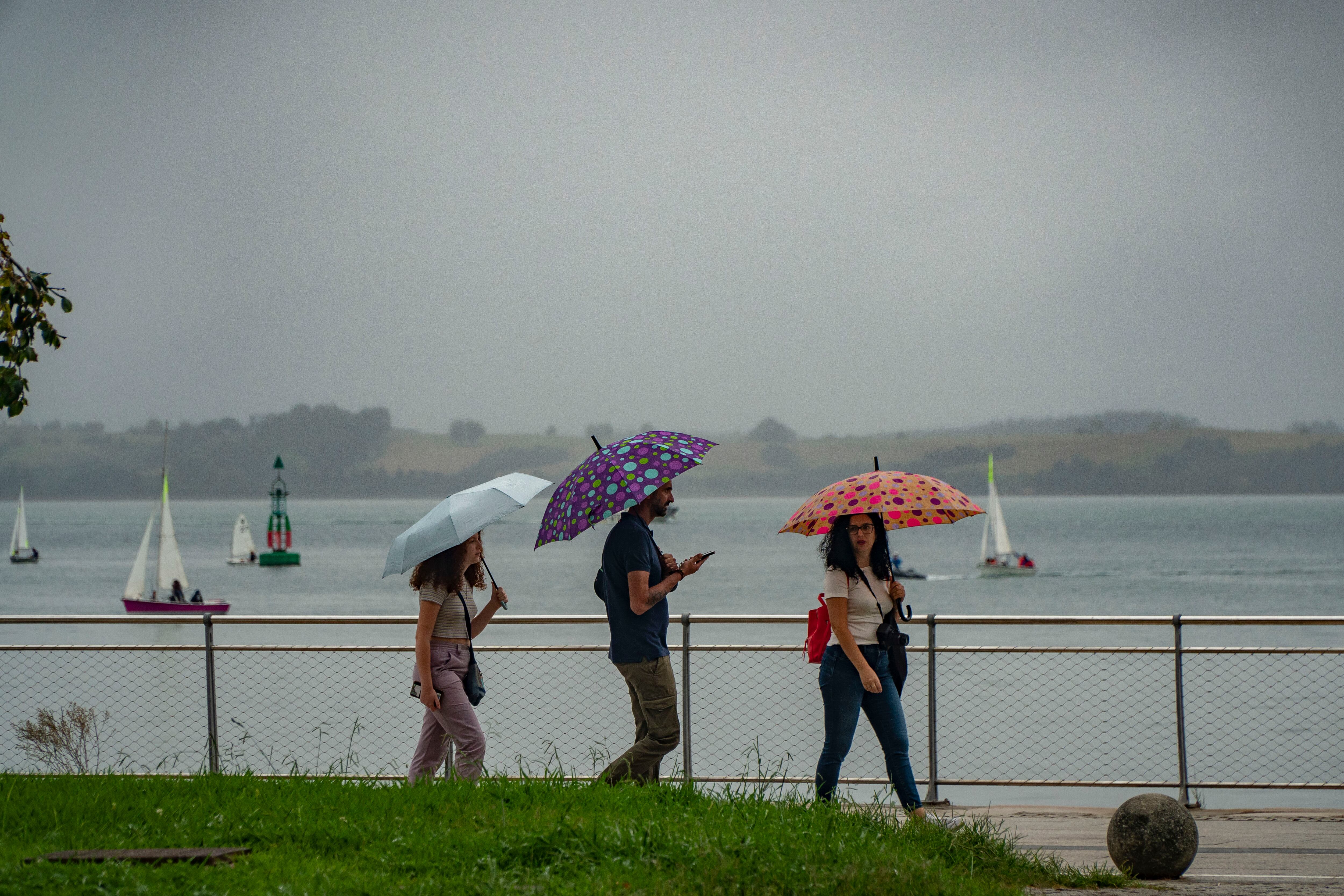 Varias personas se protegen con los paraguas de la lluvia en Santander.