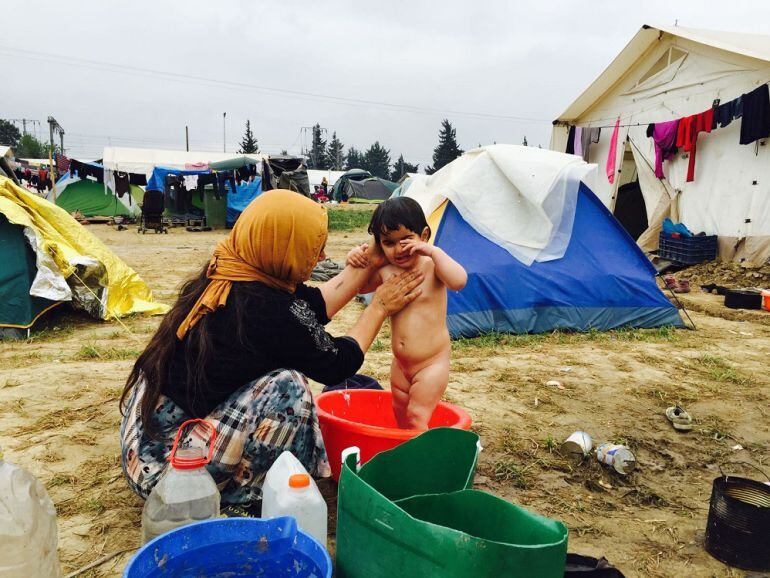 Una madre siria asea a uno de sus hijos en el campo de refugiados de Idomeni