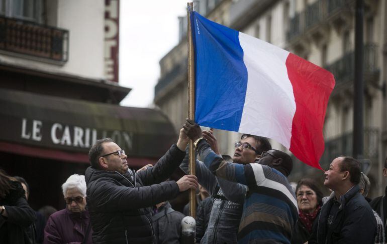 Tres personas colocan una bandera francesa ante el bar le Carillon de París, Francia.