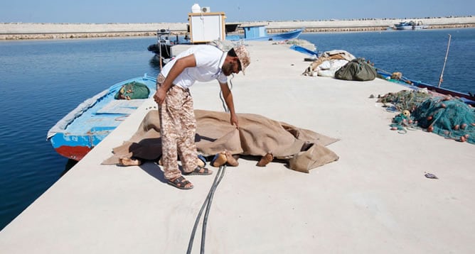 Un hombre inspecciona los cuerpos de tres inmigrantes africanos que fueron recuperados por la guardia costera de Libia, después de que su barco se hundiera frente a la ciudad costera de Garaboly, al este de Trípoli