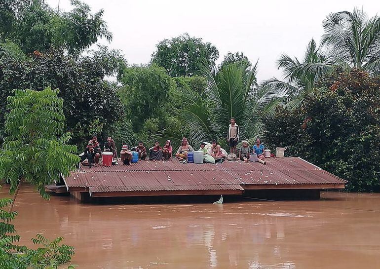 Un grupo de personas aguardan en lo alto de un tejado en una zona inundada tras el derrumbe de la presa.