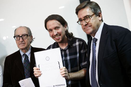 Pablo Iglesias, Secretary General of &#039;Podemos&#039; (&#039;We can&#039;), center, poses as he holds &#039;An Economic Project for the People&#039; written by Spanish economists Vincenc Navarro, left, and Juan Torres, right, in Madrid, Spain, Thursday, Nov. 27, 2014. Latest polls 