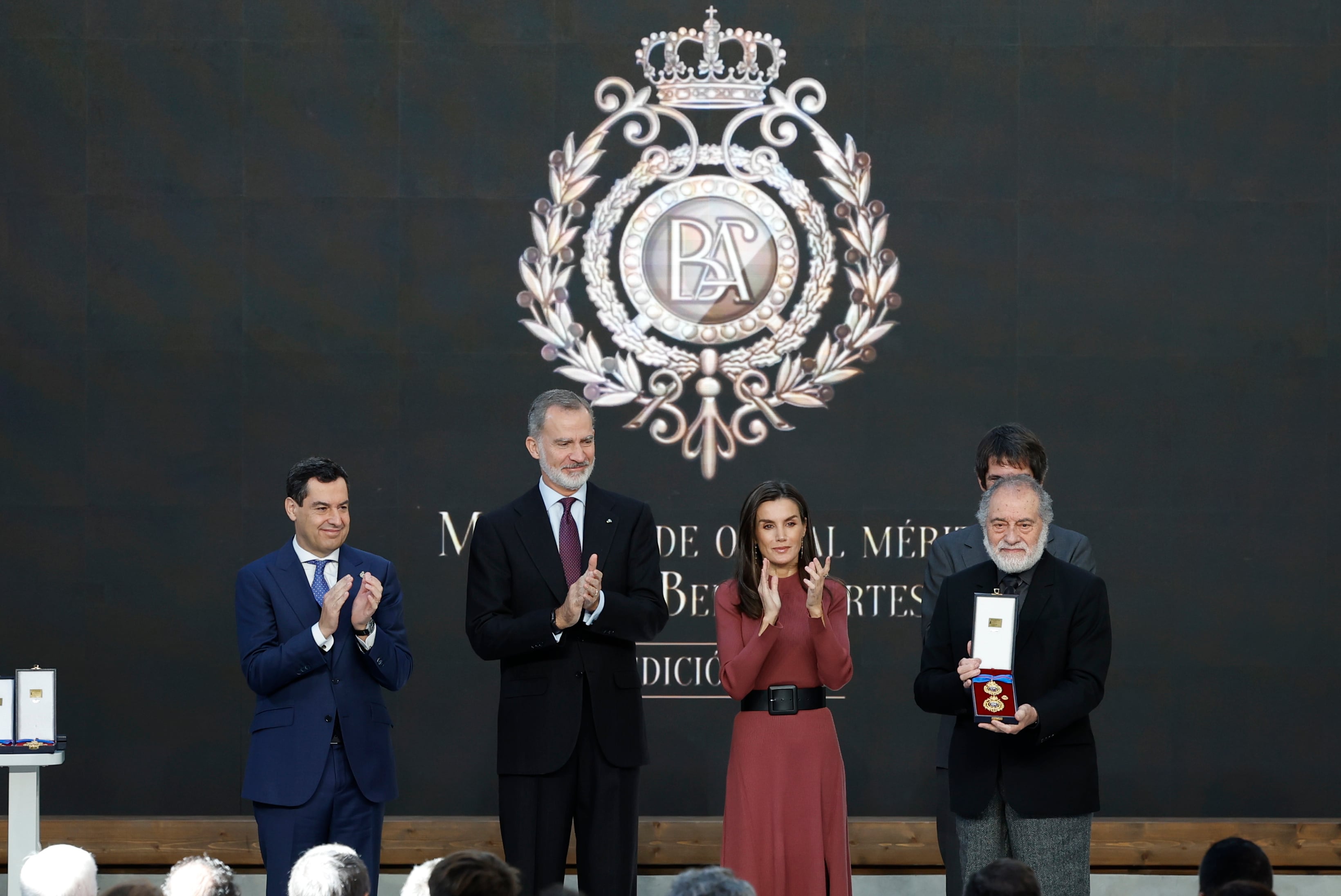 GRAFAND5159. SEVILLA, 27/11/2024.-El rey Felipe VI  y la reina Letizia, acompañados por el ministro de Cultura, Ernest Urtasun (2d), y del presidente de la Junta de Andalucía, Juanma Moreno (i), aplauden al galardonado artista y restaurador Carlos Muñoz de Pablos durante el acto de entrega de las Medallas de Oro al Mérito en las Bellas Artes 2023 concedidas por el Ministerio de Cultura a 37 personalidades e instituciones, este miércoles en la Real Fábrica de Artillería de Sevilla. EFE/Julio Muñoz
