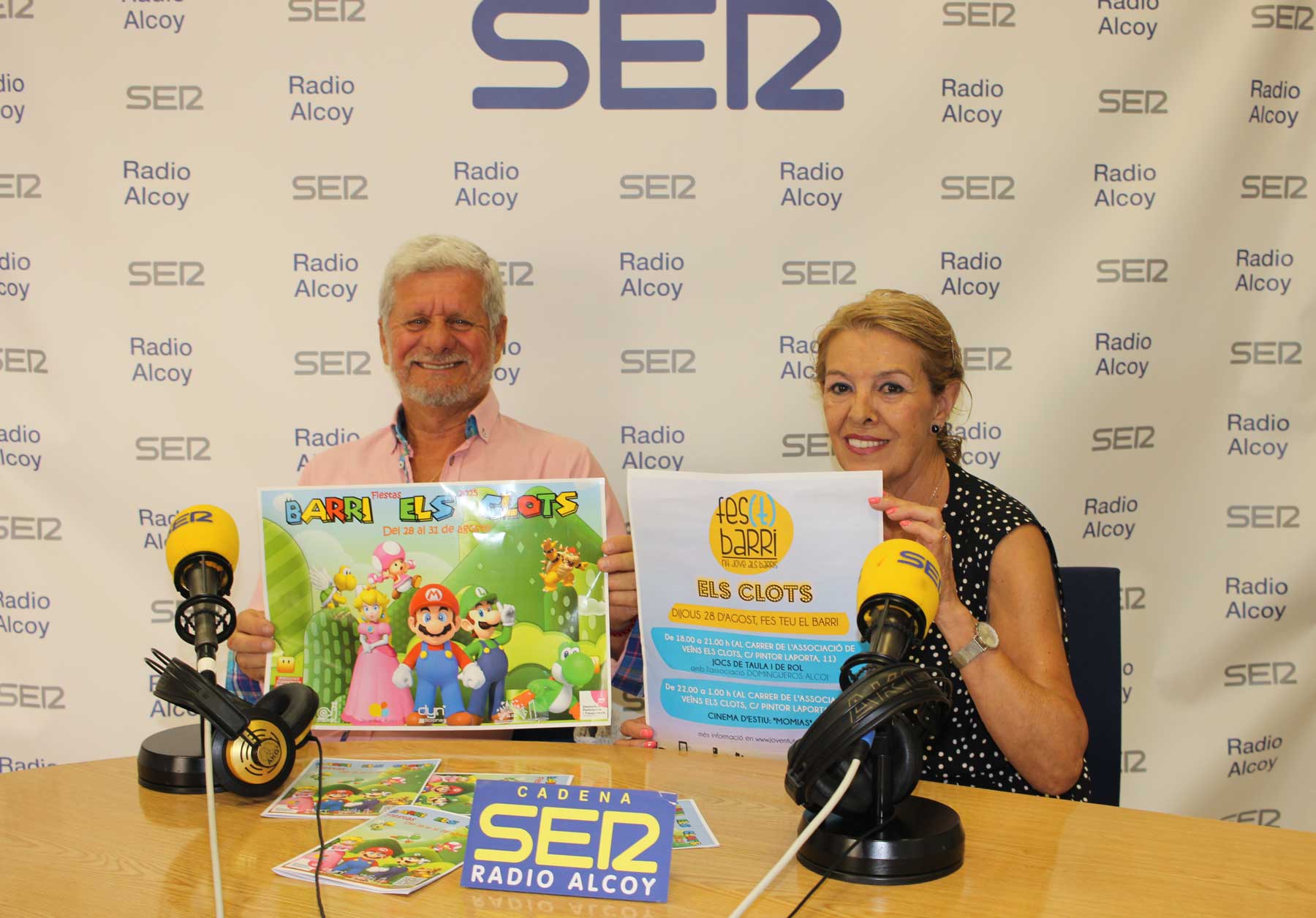 Eugenio Villahermosa y Fina Corpas, en el estudio central de Radio Alcoy, sostienen los carteles de las fiestas del barrio