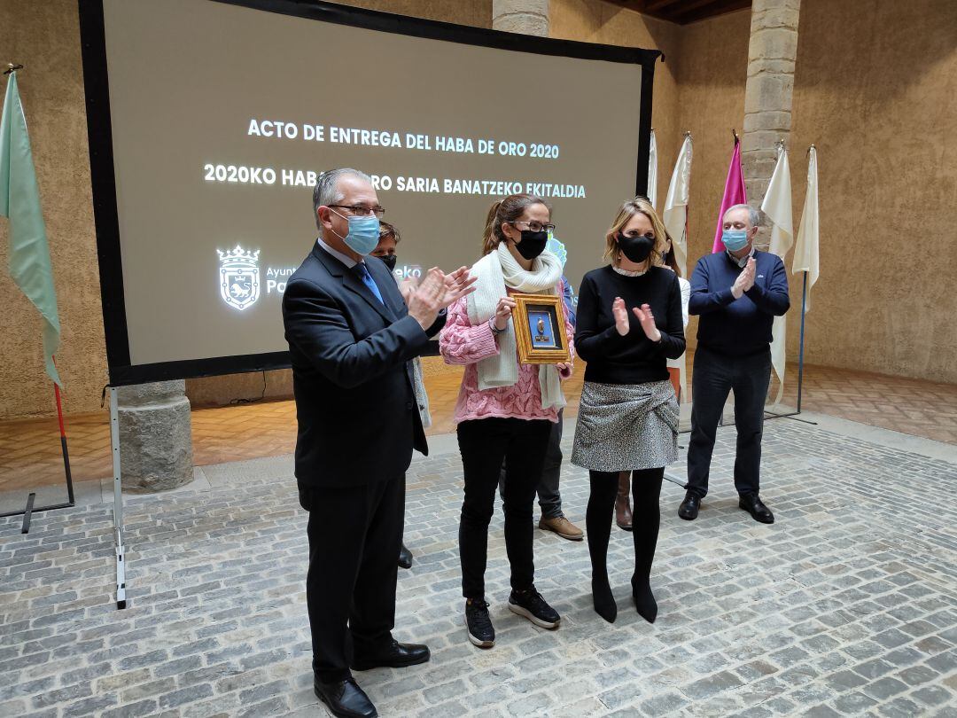 El alcalde de Pamplona, Enrique Maya, y la representante de la Asociación Cabalgata de Reyes, Mamen Sádaba, entregan el Haba de Oro a Clara Madoz, del Centro Natividad Zubieta.