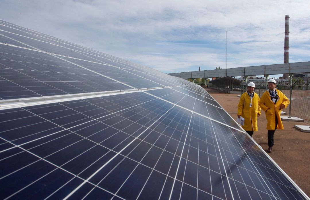Dos empleados caminan frente a paneles solares de la central eléctrica ''Chernóbil Solar'', una instalación construida cerca del refugio que protege los restos del reactor nuclear de la Unidad 4 de la central nuclear, en Chernóbil, Ucrania, hoy, 5 de octu