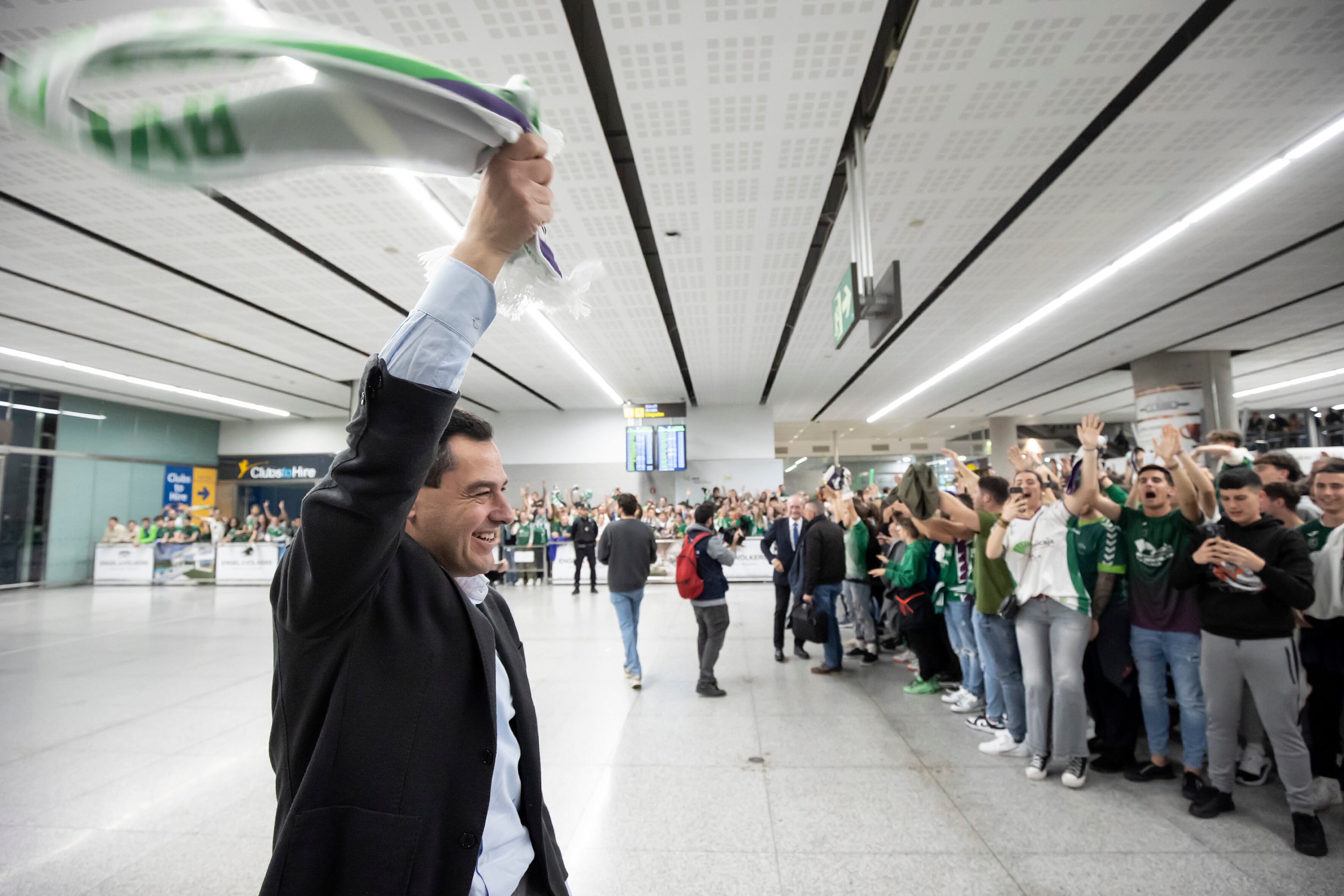AME6096. MÁLAGA (ESPAÑA), 20/02/2023.- El presidente de la Junta de Andalucía, Juanma Moreno, con aficionados de Unicaja Málaga, hoy, en el aeropuerto de la capital malacitana, el título de Copa del Rey de baloncesto que han conseguido en la final disputada ayer Domingo frente a Lenovo Tenerife en la pabellón Olímpico de Badalona. El Unicaja culminó en Badalona, ante el Lenovo Tenerife (80-83), su gran obra en la Copa del Rey, que conquistó por segunda vez en su historia tras eliminar en las rondas precedentes al Barça y Real Madrid, un gesta que ningún equipo había hecho nunca en la era ACB. EFE/Daniel Pérez

