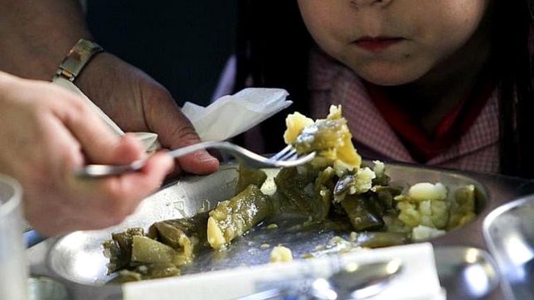 Un monitor da de comer a una niña en un comedor de una escuela pública