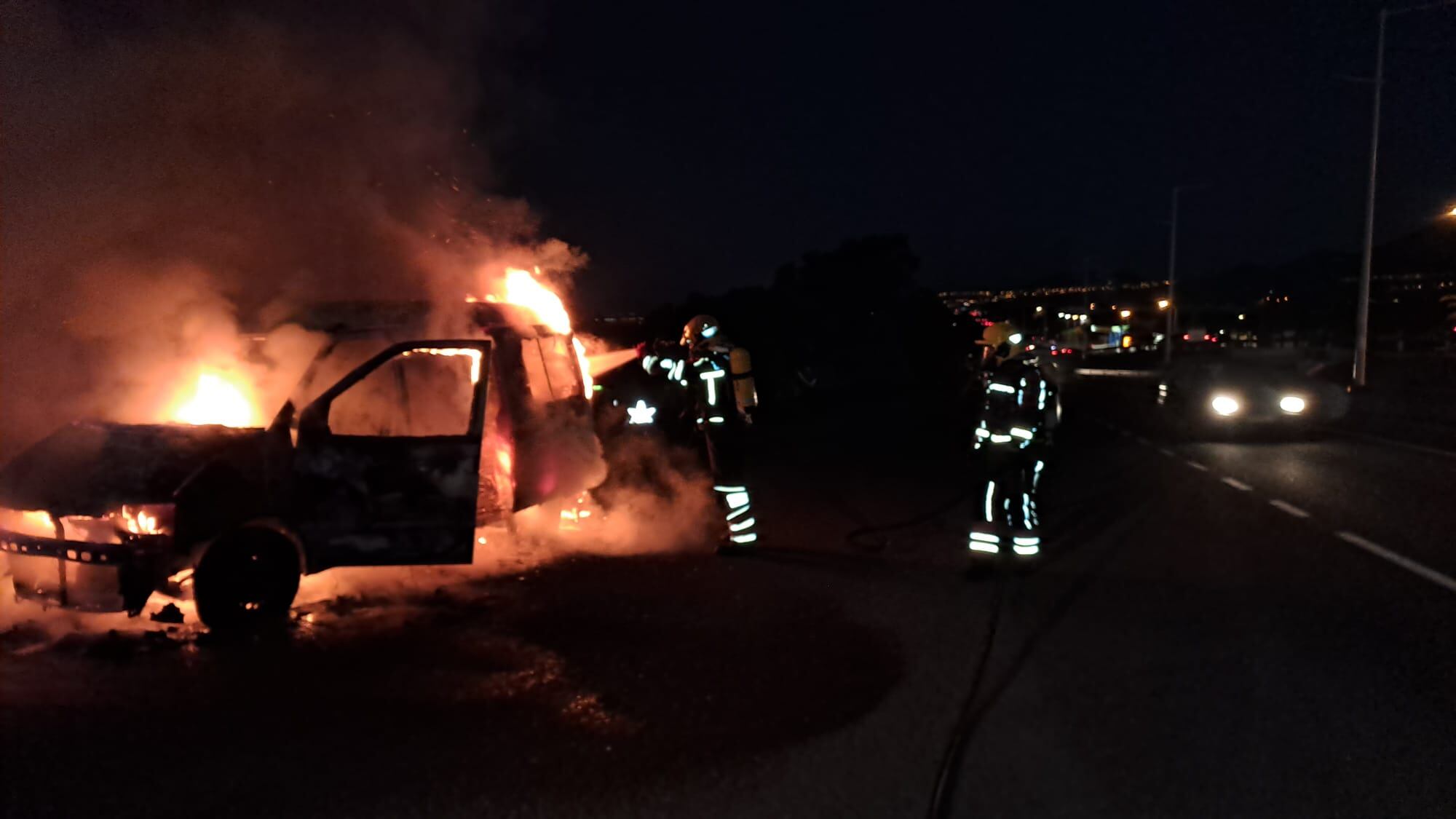 Bomberos actuando junto a la furgoneta incendiada.