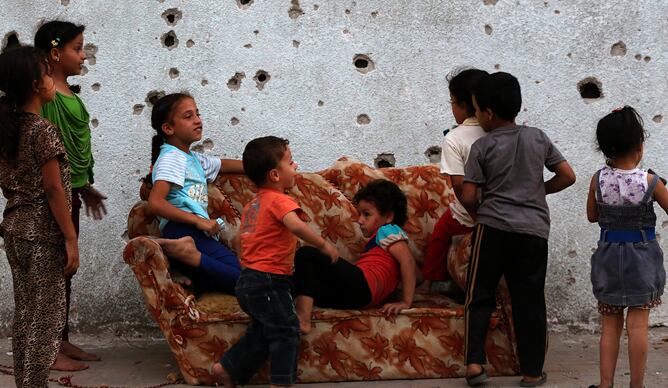 Niños palestinos juegan en un sofá, junto a un muro baleado en el barrio de Al Shejaeiya al este de la ciudad de Gaza