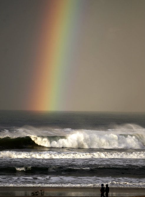 Dos personas caminan bajo un arcoiris en la playa de La Zurriola de San Sebastián