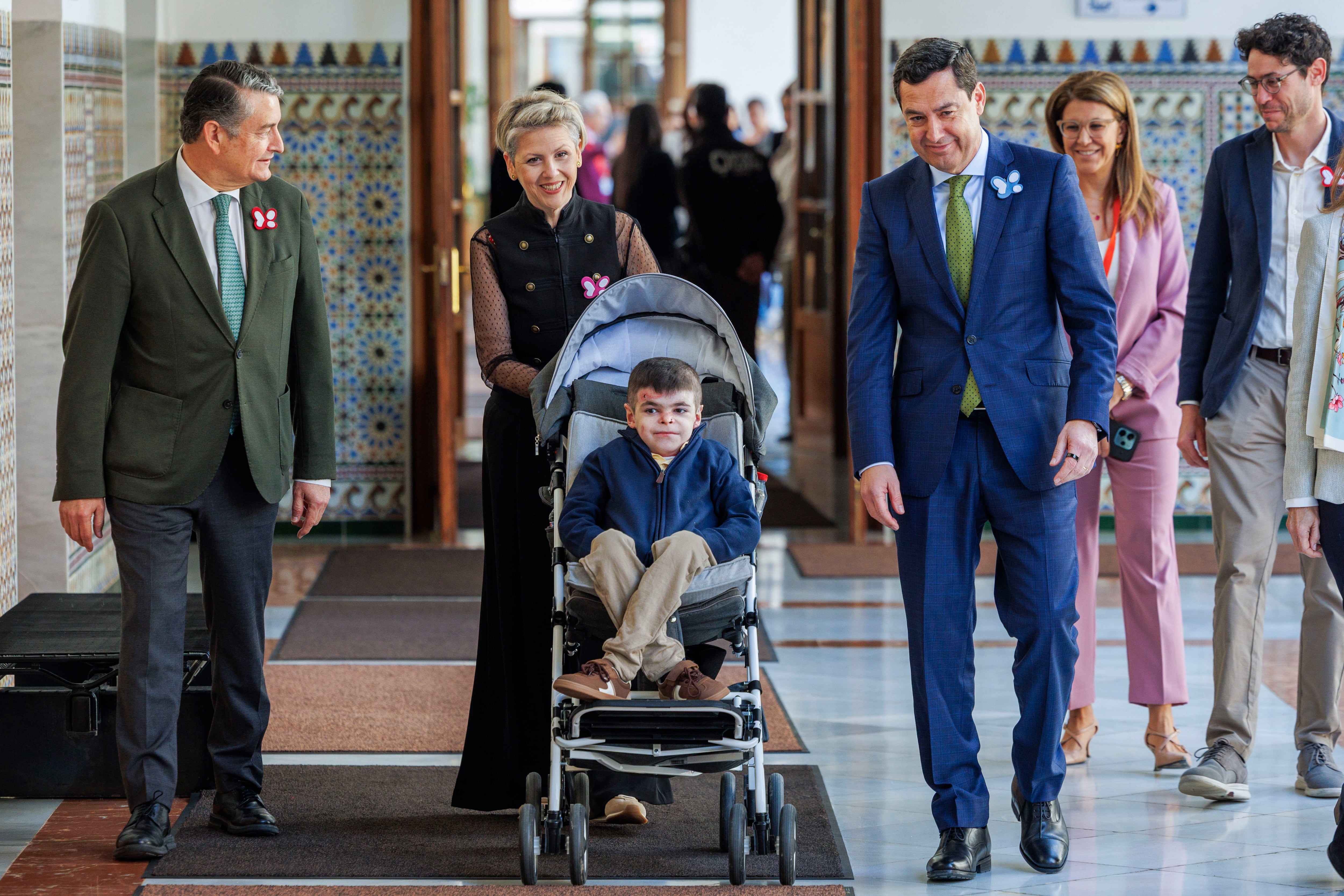 SEVILLA, 12/03/2026.- El presidente de la Junta de Andalucía, Juanma Moreno, llega a la sesión de control del Parlamento andaluz acompañado de Leo, un niño de 12 años de Sevilla que contó esta semana su caso en la Eurocámara. Moreno, ha anunciado este jueves que buscará la fórmula para asumir el coste del tratamiento pionero que mitigará los efectos de la epidermólisis bullosa distrófica, enfermedad conocida como de la 'piel de mariposa'. EFE/ Julio Muñoz
