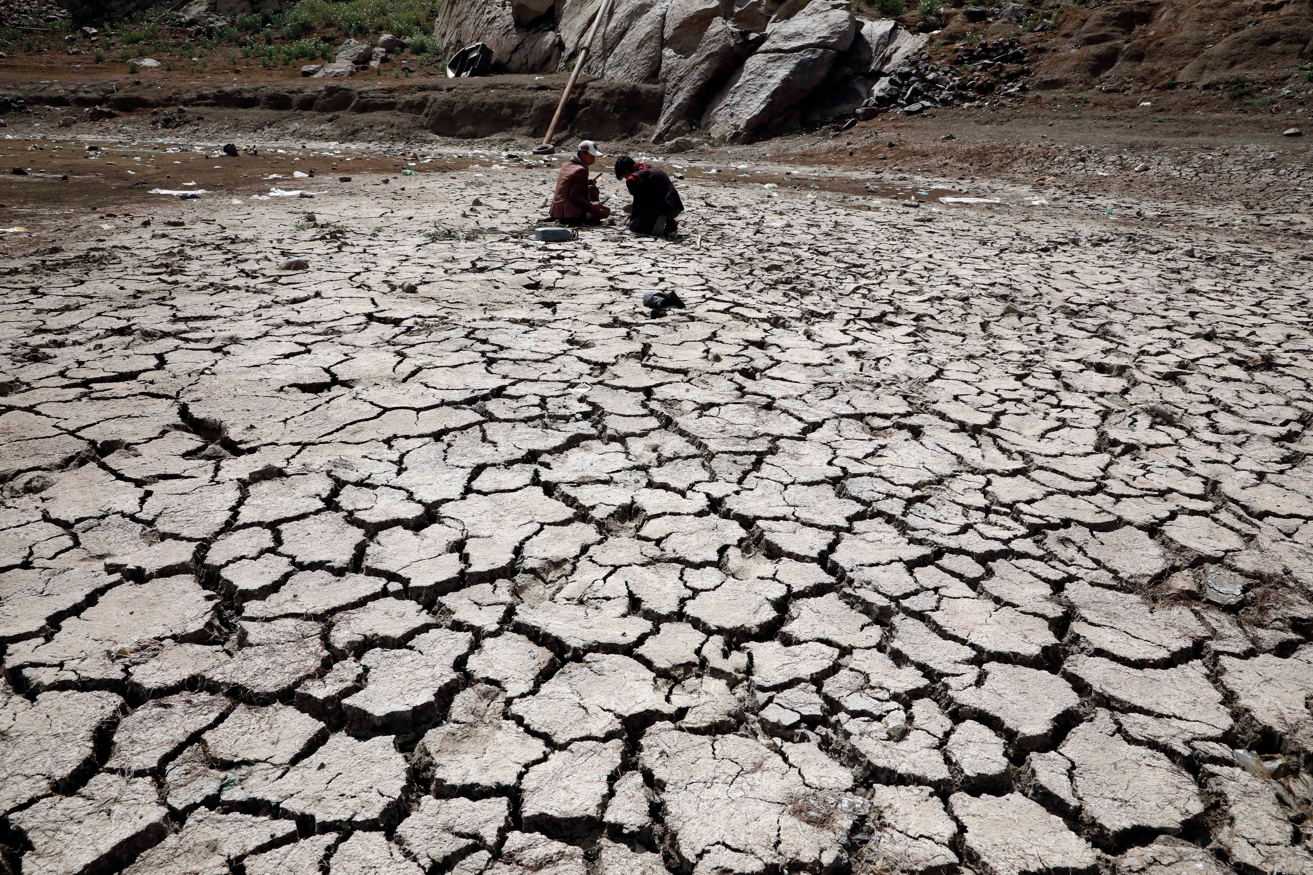 Personas sentadas en el lecho de un embalse afectado por la sequía en las afueras de Saná (Yemen)