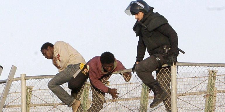 GRA072 MELILLA, 22/10/2014.- Un agente de Policía junto a dos de los ochenta inmigrantes que están encaramados desde primera hora a la valla de Melilla, fronteriza con Marruecos, tras el último intento de entrar en la ciudad autonóma protagonizado por var