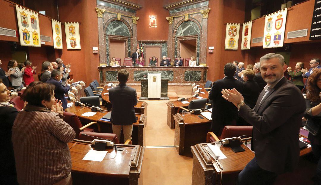 Rosa Peñalver en su último discurso como presidenta de la Asamblea Regional. En primer plano, Óscar Urralburu (Podemos) sonríe y aplaude las palabras de Peñalver