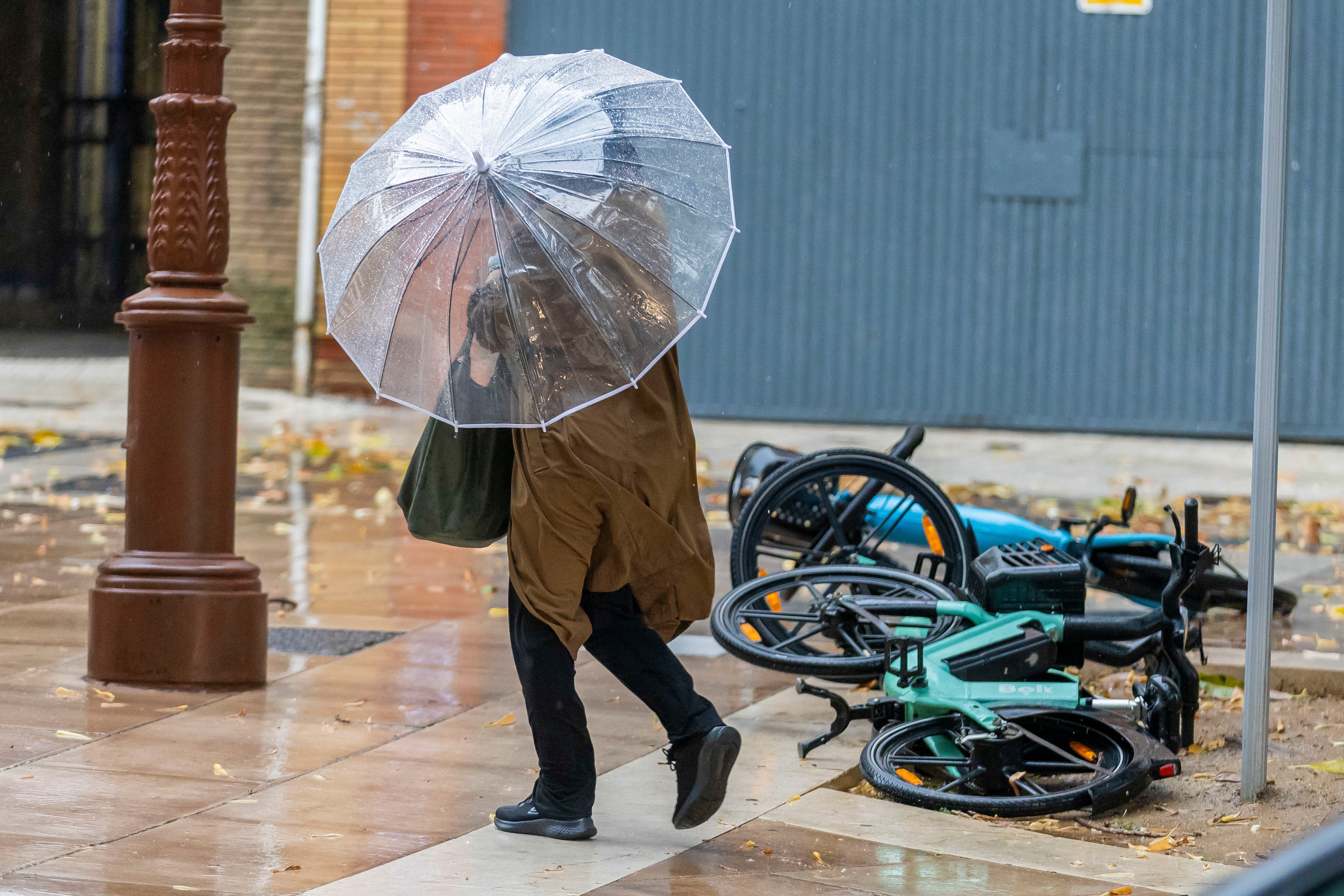 Una mujer con paraguas pasa ante unas bicicletas caídas en Huelva este miércoles.