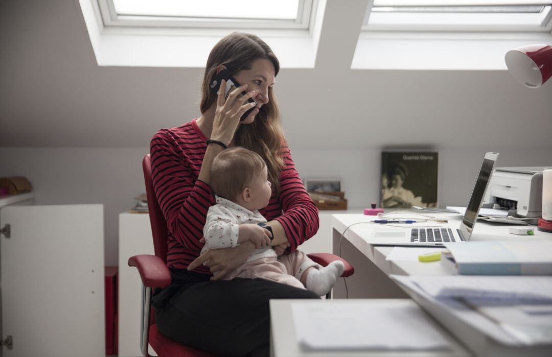 Una mujer teletrabaja desde su casa mientras sostiene a su bebé durante el confinamiento en Madrid.