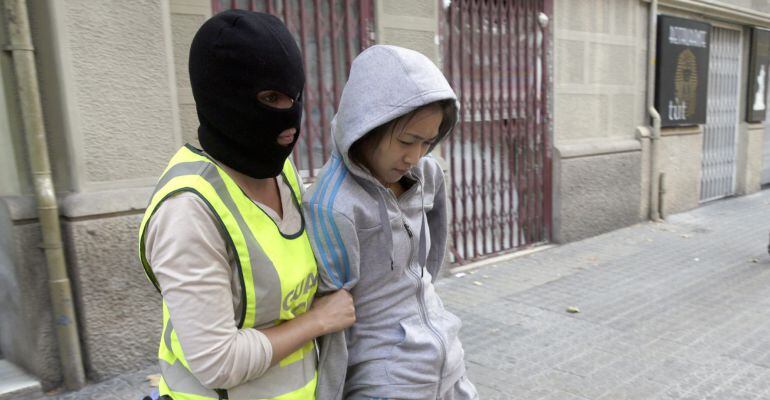 B01. BARCELONA, 01/07/2015.- Una agente de la Guardia Civil custodia a una de las detenidas en la operación que un centenar de efectivos de este cuerpo están llevando a cabo esta mañana contra una red de delincuentes de origen chino que se dedicaban a facilitar la inmigración ilegal, a la trata de seres humanos, la falsificación de documentos y el tráfico de drogas. EFE/Alberto Estévez