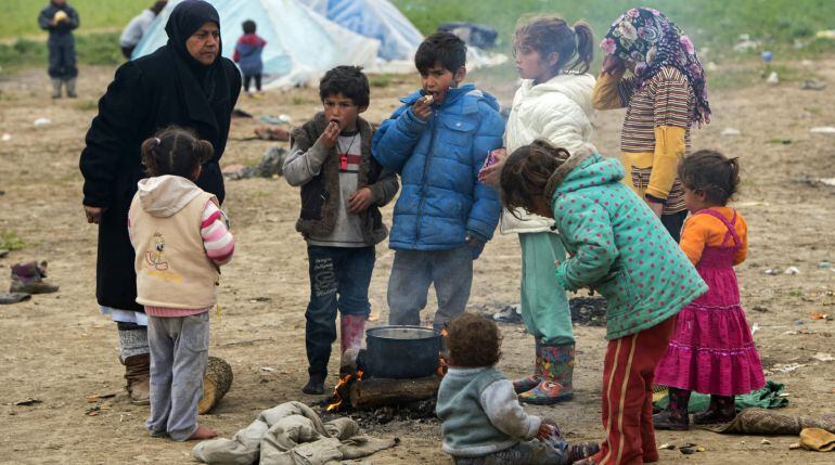 Refugiados comen junto a una hoguera en el campo de refugiados de Idomeni (Grecia)
