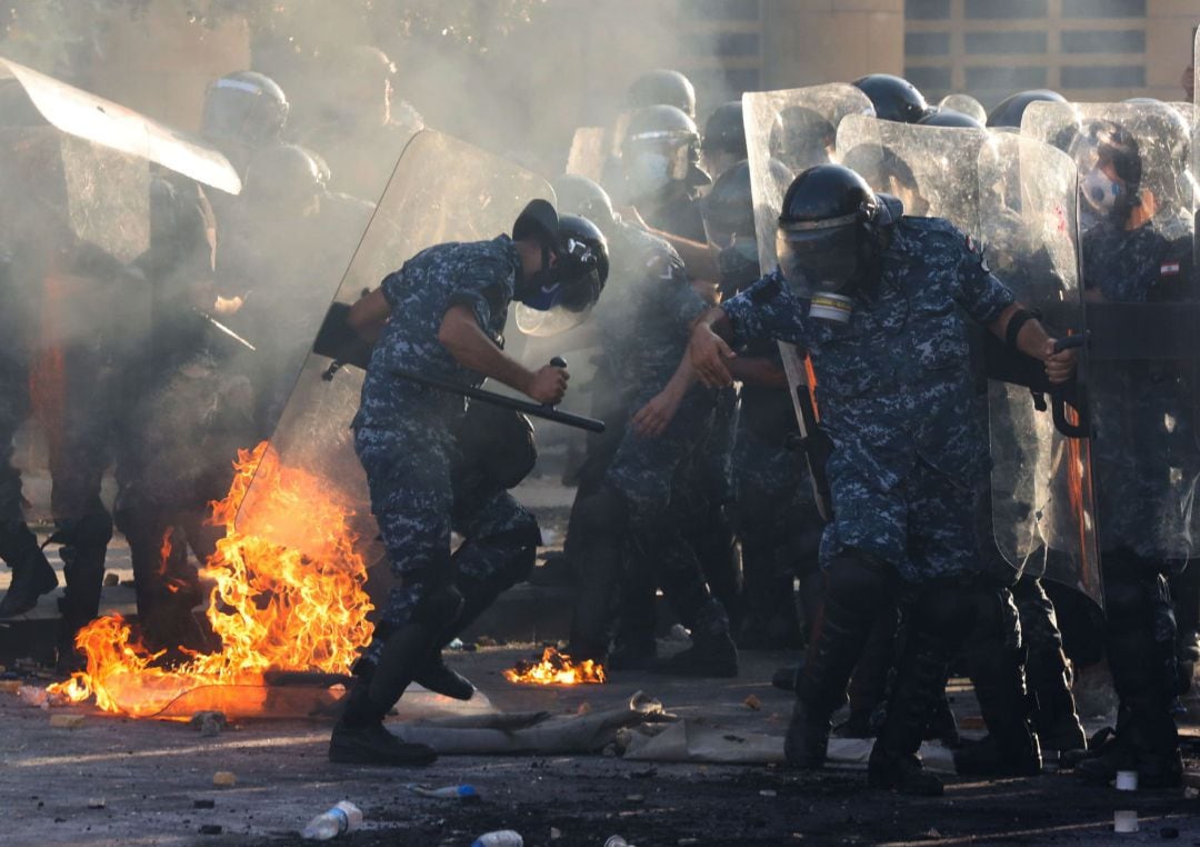 La policía antidisturbios libanesa intenta apagar un incendio cercano durante los enfrentamientos con manifestantes contra el gobierno en una protesta en Beirut, Líbano