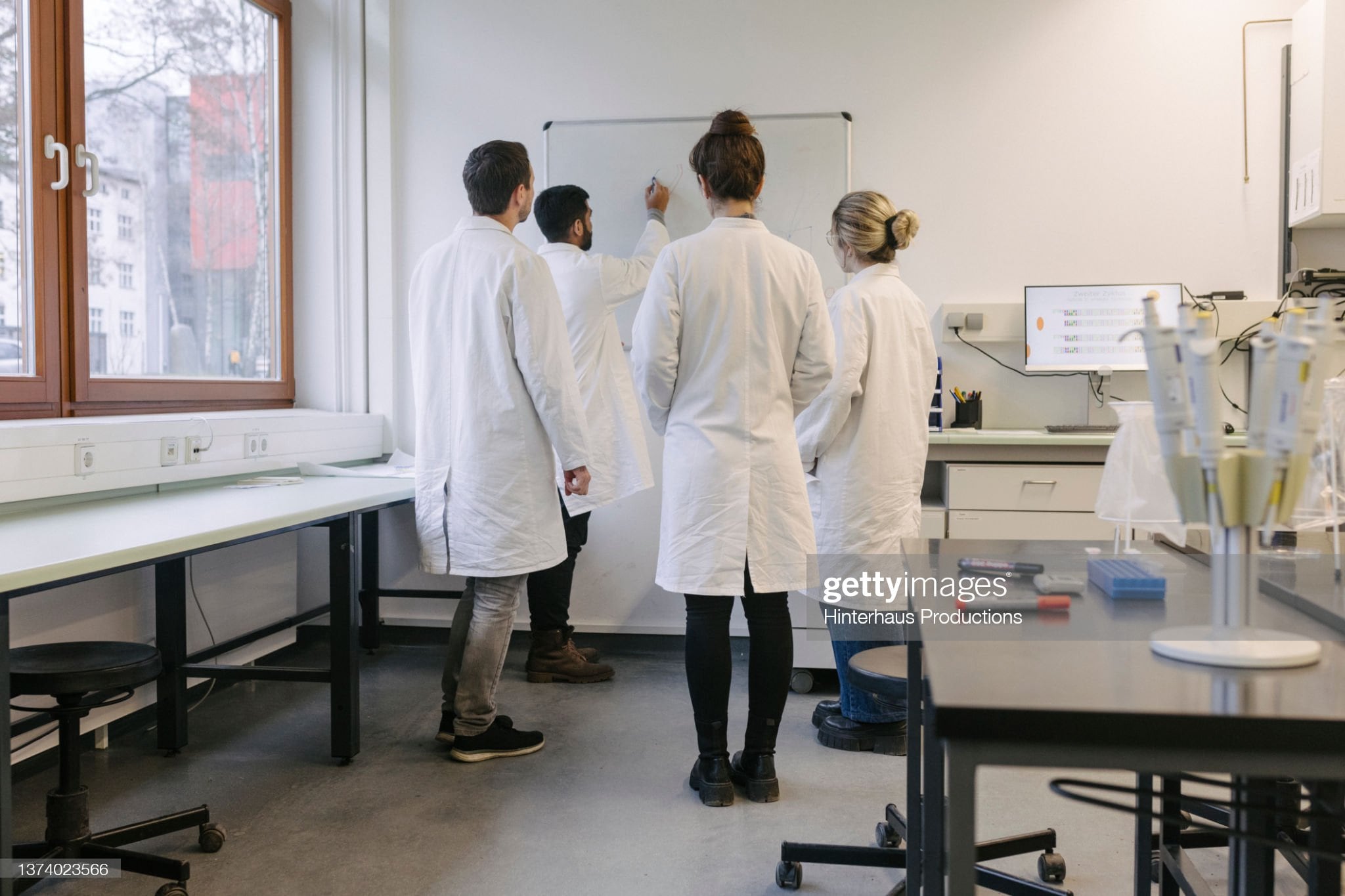 A group of medical students discussing some work while huddled around a whiteboard at the lab together.