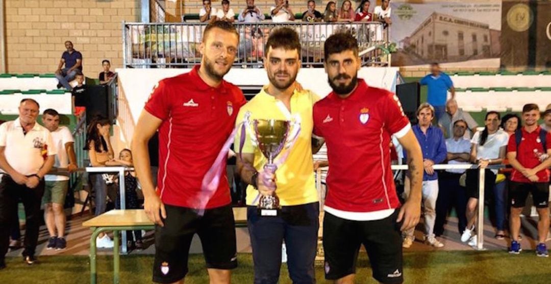 El alcalde de Villargordo, Miguel Manuel García (centro), acompañado de los futbolistas del Real Jaén Ramón (a su derecha) y Juanma Espinosa (a su izquierda).