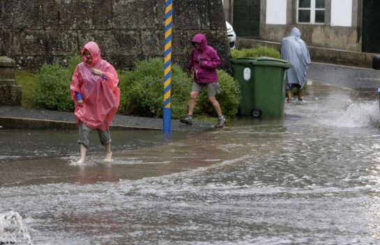 Tres peregrinos pasan por una calle inundada este lunes en Santiago de Compostela.