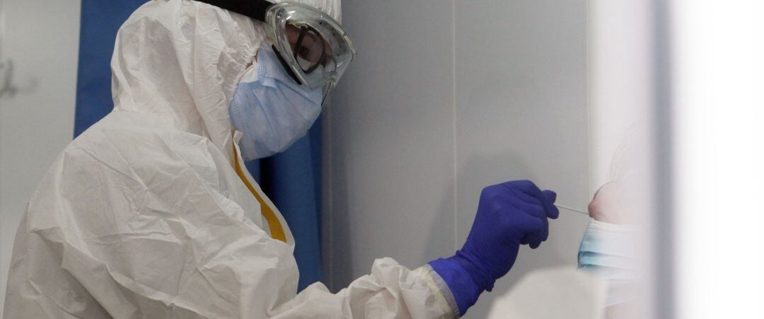 Un sanitario protegido con gafas, mascarilla y traje, practicando una prueba de COVID-19.