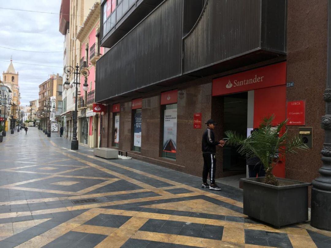 Una oficina bancaria en el centro de Lorca con una persona guardando turno en la puerta