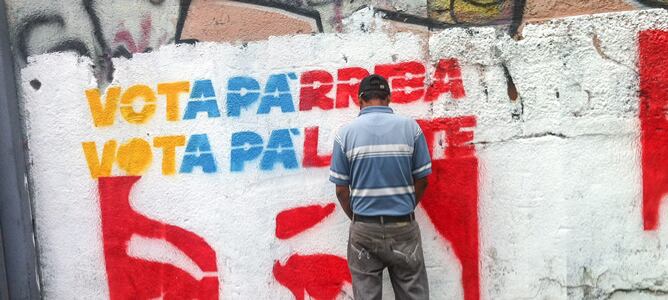 Un hombre orina frente a un muro con propaganda de la campaña electoral venezolana.