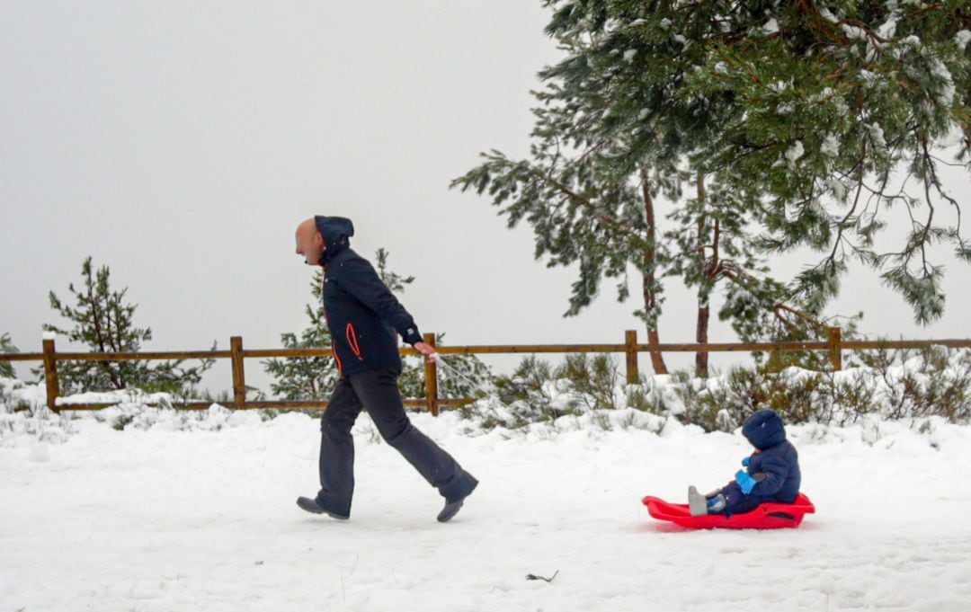 Un padre tira del trineo de su hijo durante el temporal de nieve en la Sierra de Madrid.