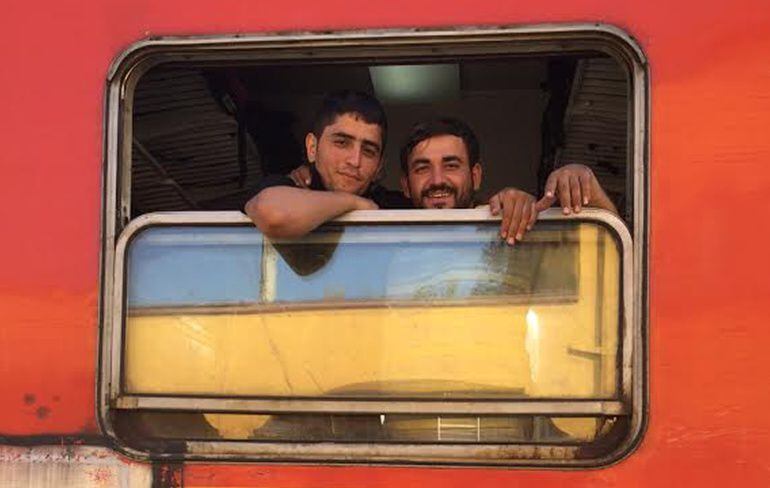 Dos refugiados sirios sonríen desde el interior del tren que les cruzará a Serbia desde Macedonia