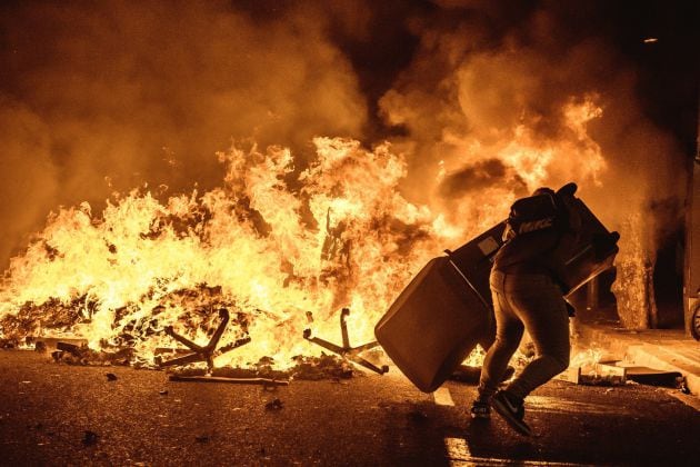 Un manifestante lanza un contenedor a una hoguera en medio de las protestas